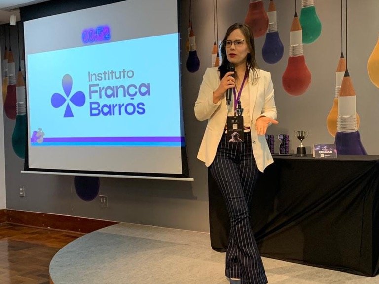 Palestrante no palco com microfone, ao lado do telão que exibe a marca Instituto França Barros