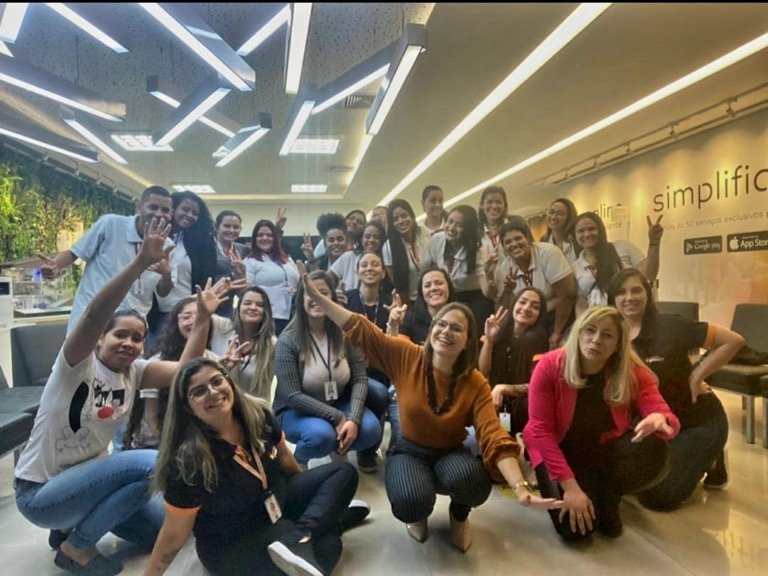 Turma reunida na recepção de uma empresa comemora ao final do treinamento, com gestos de vitória